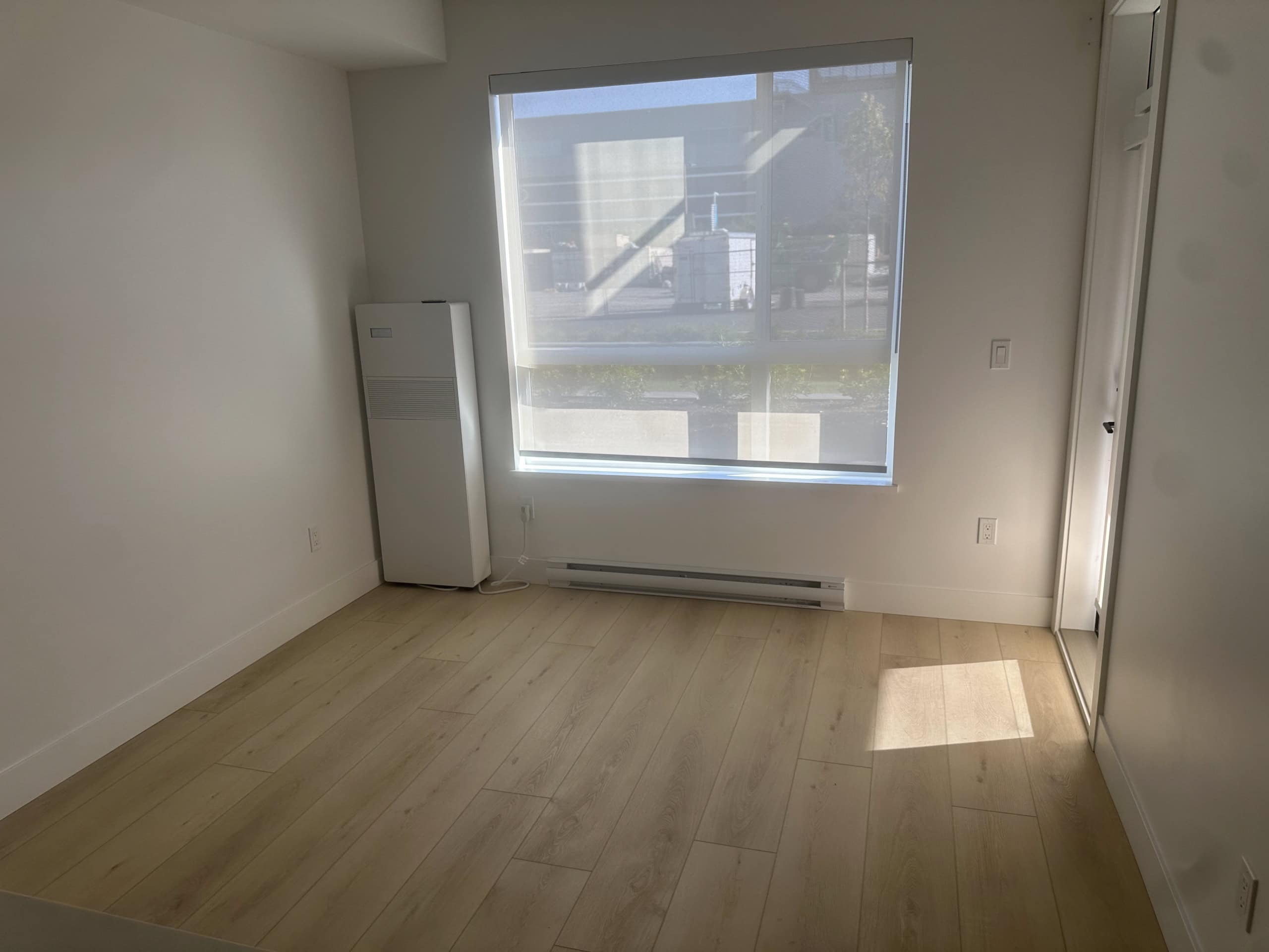 Bright modern apartment room with large window and natural light, featuring white walls, hardwood flooring, and a built-in closet, ideal for Vancouver real estate buyers and investors.