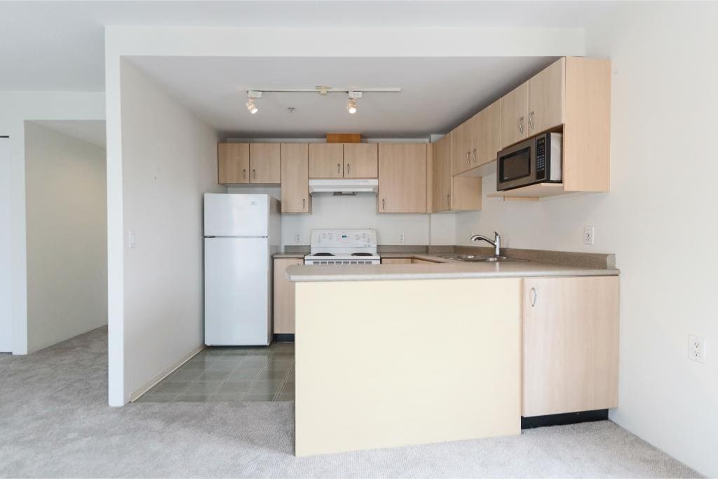 Modern apartment kitchen with white appliances, light wood cabinets, and neutral decor, perfect for Vancouver real estate buyers.
