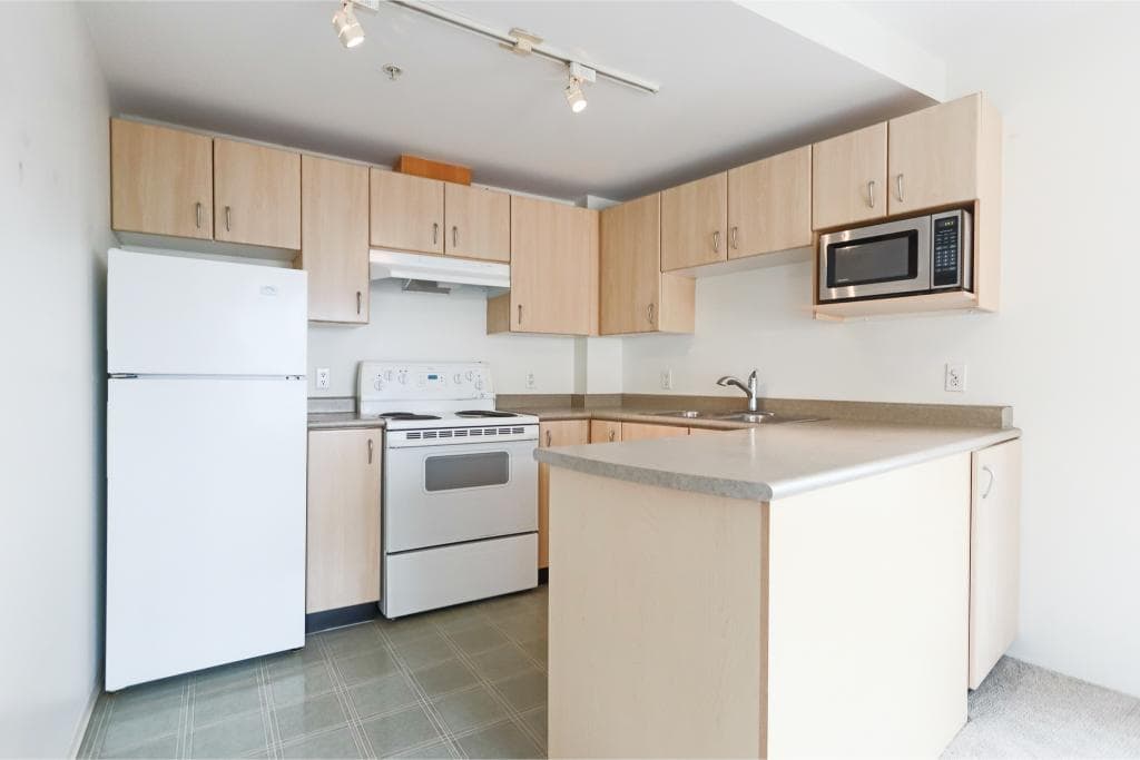 Kitchen with white refrigerator, stove, microwave, and beige cabinets in a condo or apartment in Victoria, BC.