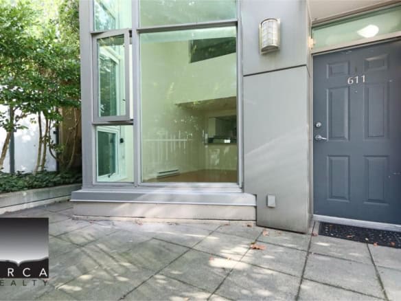 Modern townhouse entrance with gray door and large glass window, landscaped greenery, and outdoor patio in Vancouver, BC.
