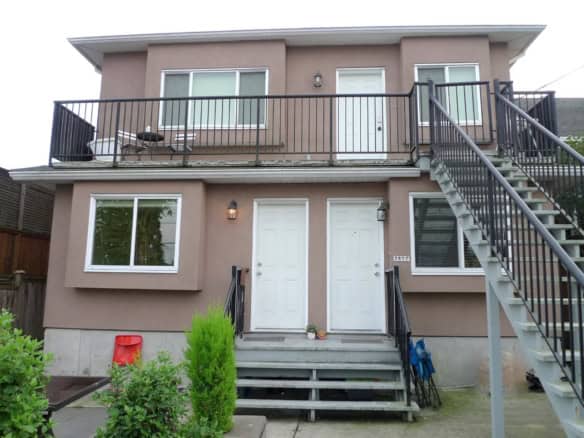 Modern two-storey beige duplex with front entrance, outdoor balcony, and metal staircase, ideal for Vancouver Island real estate investment and residential living.