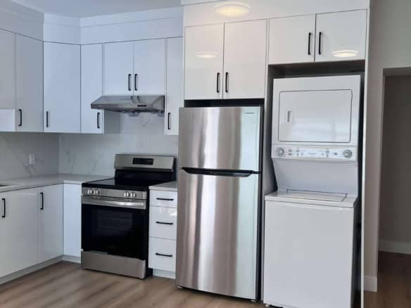 Modern kitchen with stainless steel appliances, white cabinetry, and light wood flooring, featuring a refrigerator, stove, and washer/dryer in a contemporary Orca Realty Inc. property.