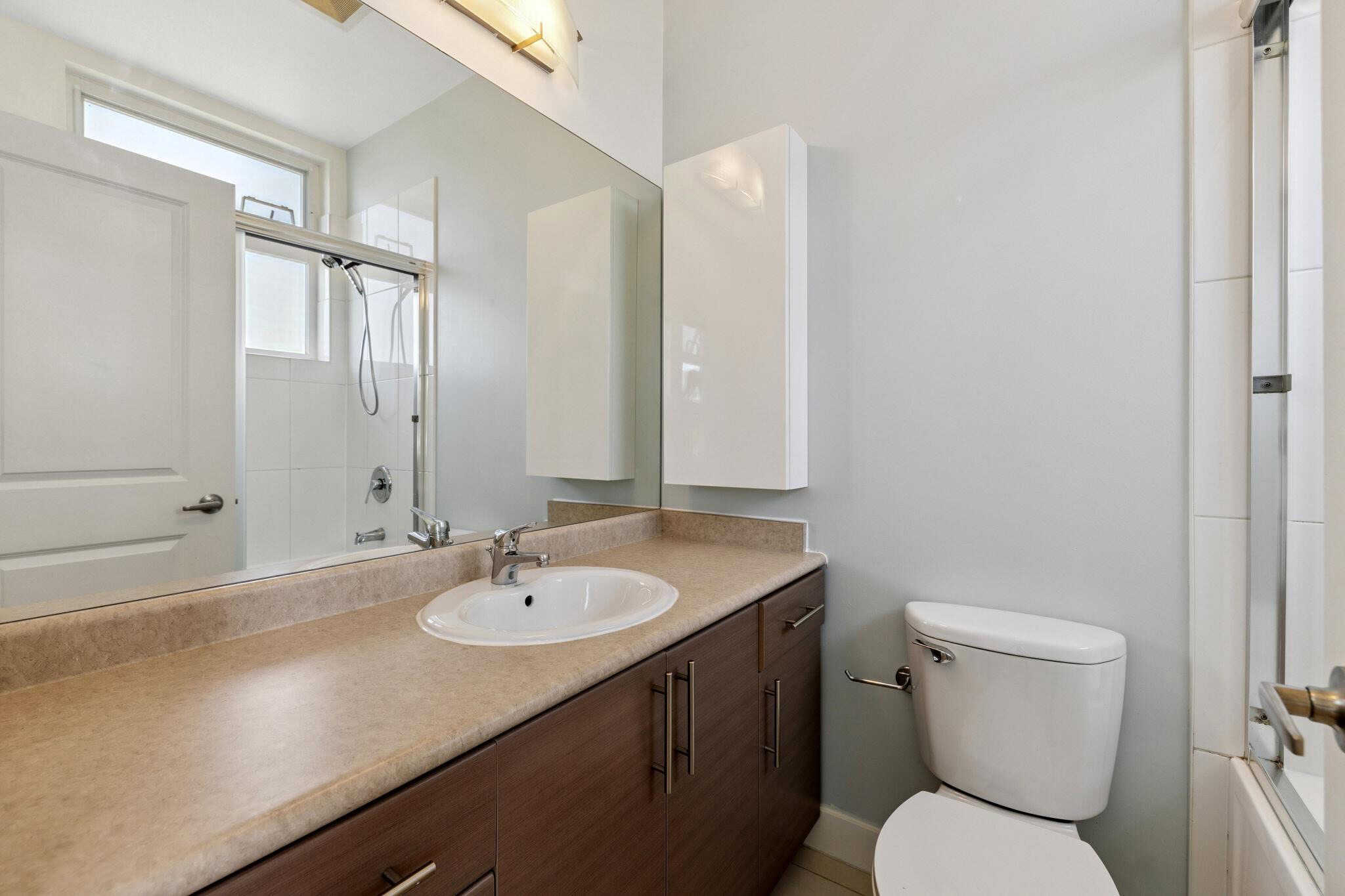 Bright bathroom with vanity, sink, mirror, and shower/tub combo, featuring modern fixtures and ample natural light; perfect for Vancouver Island home comfort.