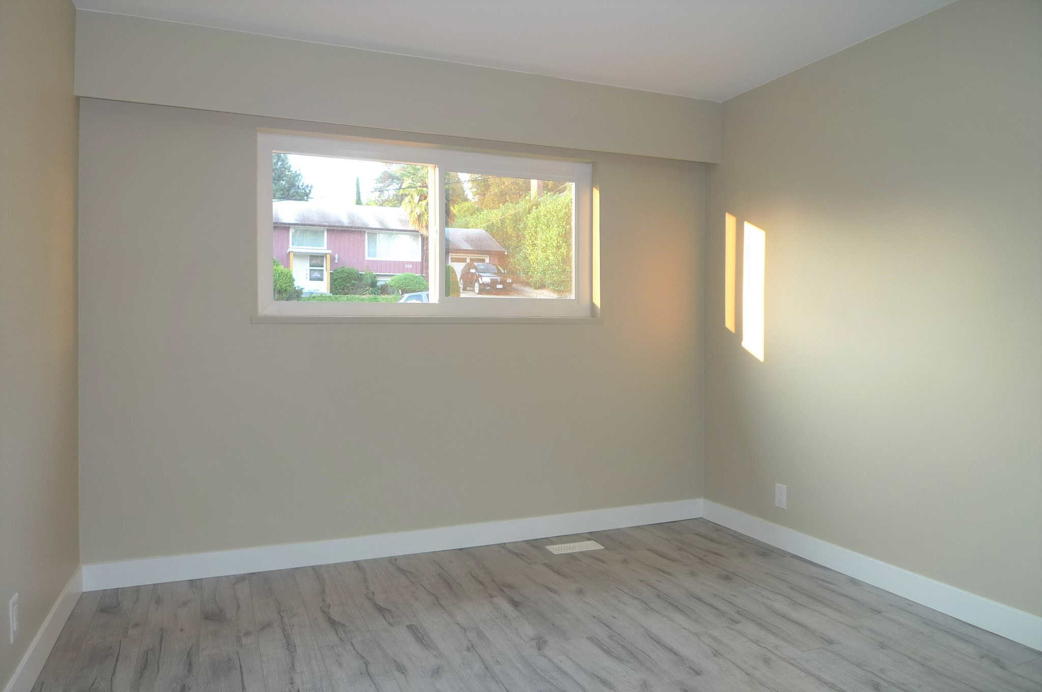 Bright empty room with large window, modern light wood flooring, neutral beige walls, ideal for Vancouver-area real estate listings.