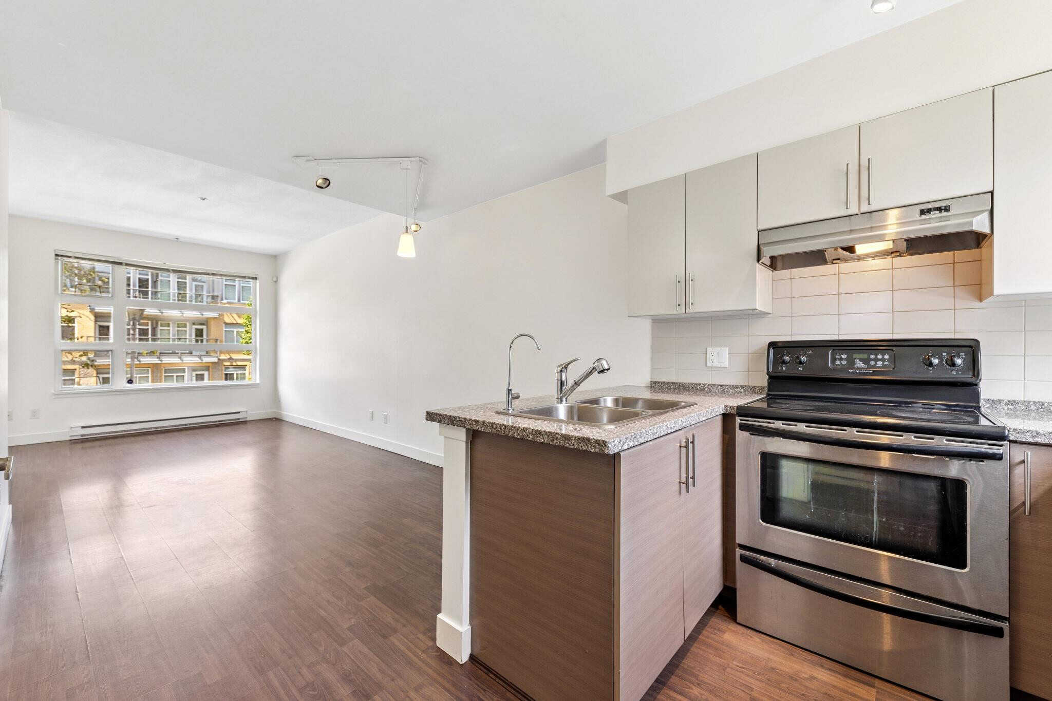 Spacious modern apartment kitchen and living area in Vancouver, featuring stainless steel appliances, hardwood floors, and large windows with city views. Perfect for urban living and real estate investment.