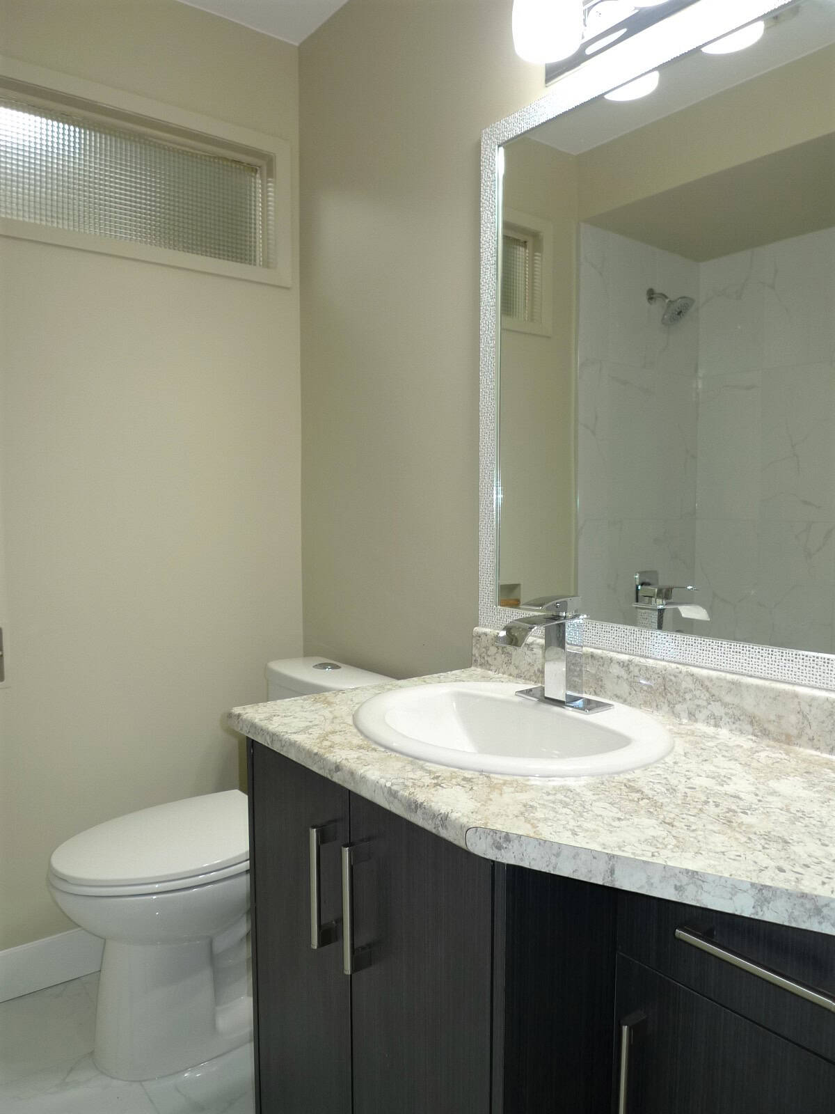 Modern en-suite bathroom with marble countertop, stylish black vanity, and a sleek large mirror; featuring a toilet and a walk-in shower with marble tiles, ideal for Vancouver real estate listings.