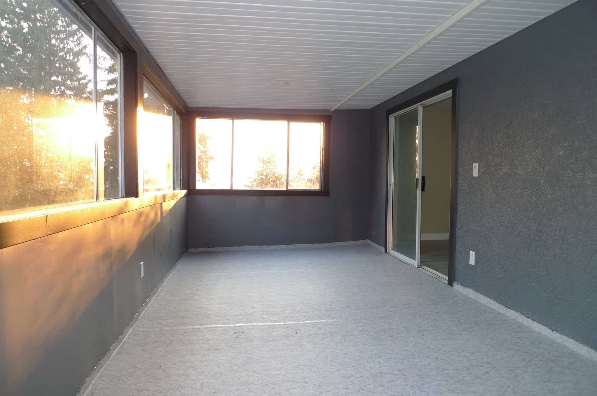 Bright enclosed balcony with large windows and sliding glass door, overlooking a scenic outdoor view, ideal for relaxing and enjoying natural sunlight.
