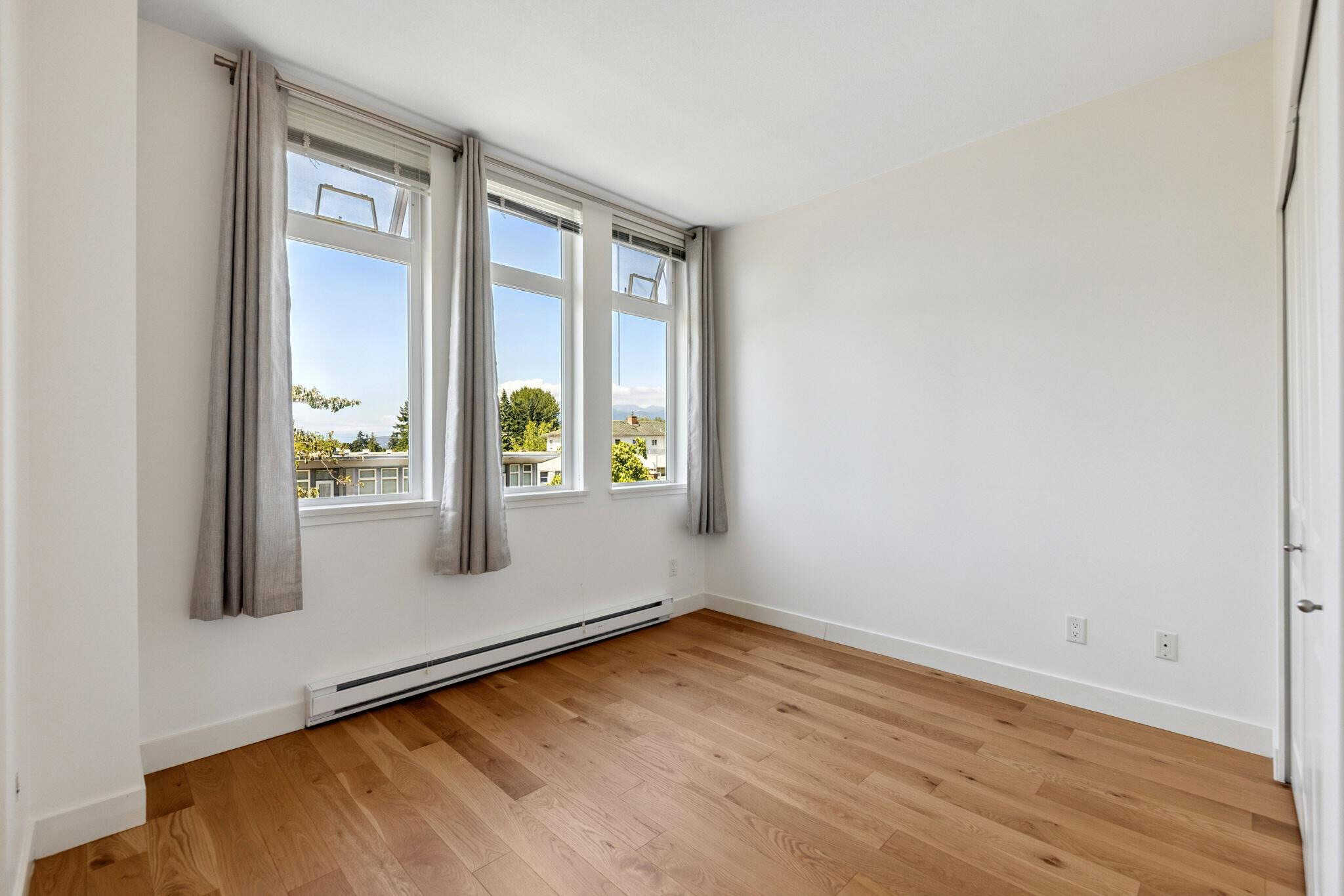 Bright bedroom with large windows, natural light, hardwood floors, and cozy curtains, ideal for Vancouver homes.