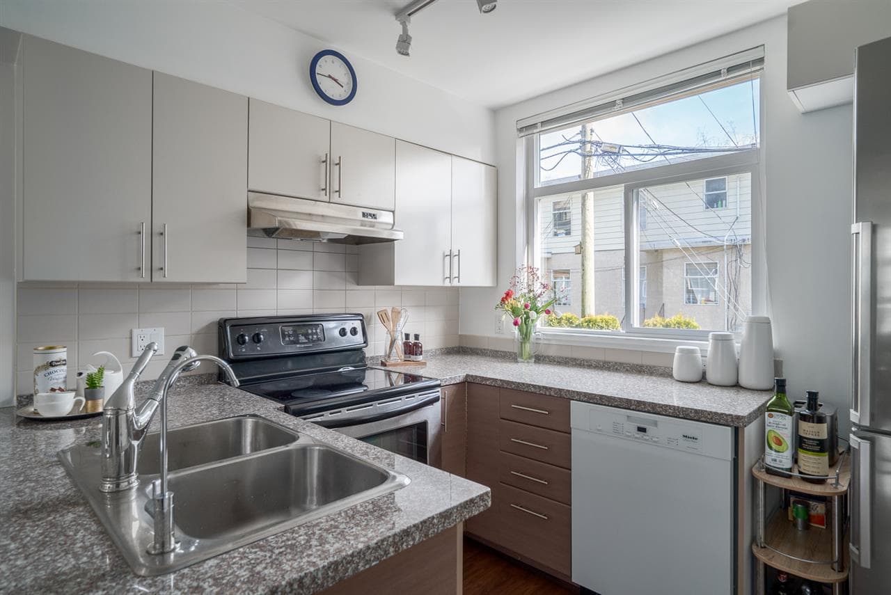 Bright modern kitchen with stainless steel appliances, granite countertops, and a large window bringing in natural light, ideal for homebuyers seeking stylish and functional Vancouver real estate.