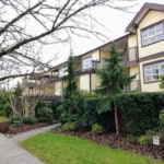 Spacious multi-family residential building with lush landscaping, tall evergreen trees, and welcoming walkways, located in a prime neighbourhood for real estate investment in Vancouver, BC.