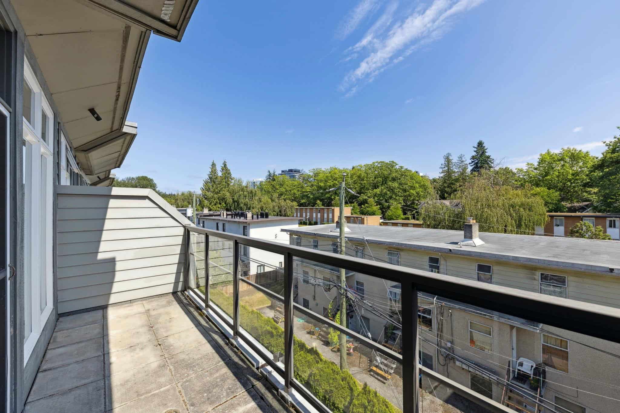 Spacious balcony overlooking tree-lined neighbourhoods and rooftops with clear blue sky, ideal for outdoor living and enjoying Vancouver Island's natural beauty.