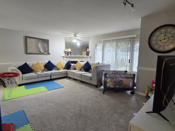 Bright and spacious living room with neutral decor, comfortable sectional sofa with colorful pillows, large windows with vertical blinds, and a cozy family area perfect for relaxation and family gatherings.