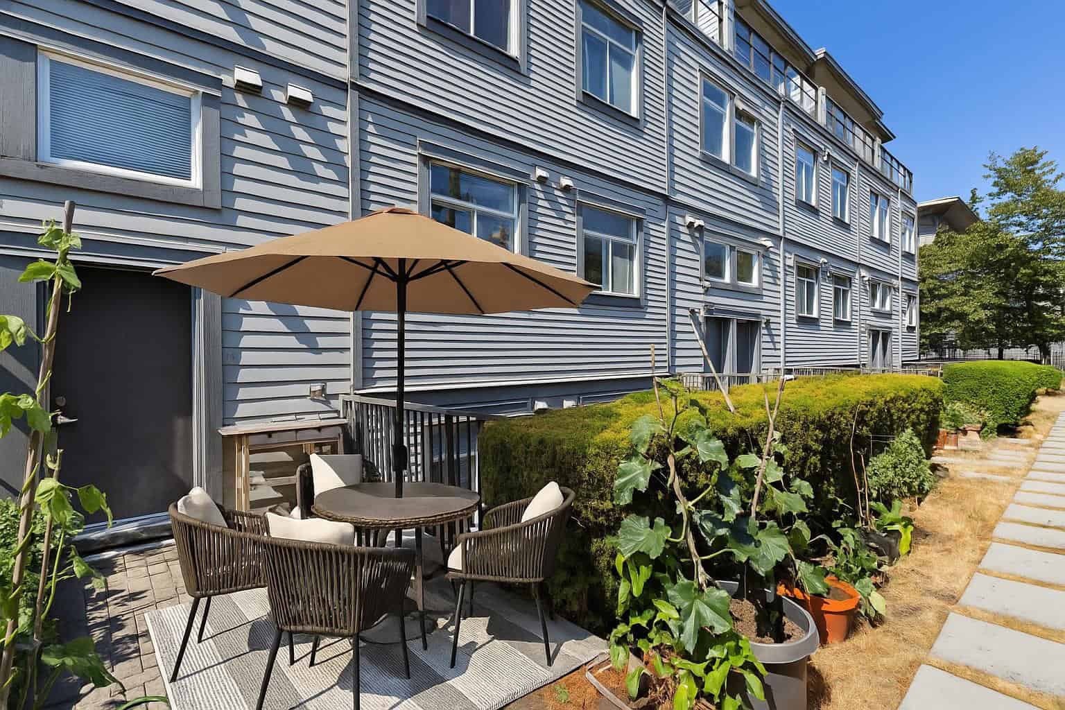 Bright outdoor patio area with a table, chairs, and umbrella in the backyard of a modern apartment building, perfect for relaxation and outdoor living in Vancouver.