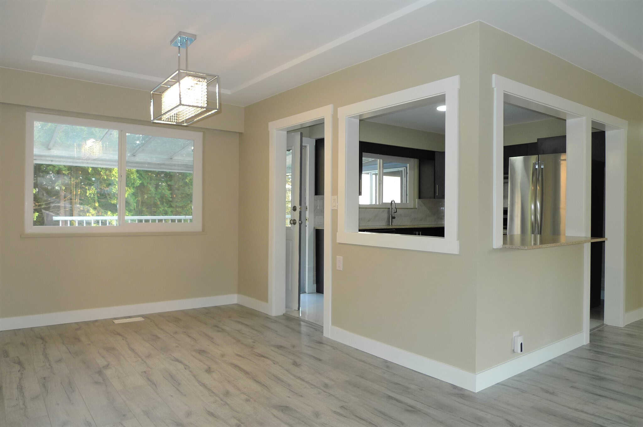 Bright, modern open-concept living space with large windows, stylish lighting fixture, and seamlessly connected kitchen, ideal for Calgary homes.