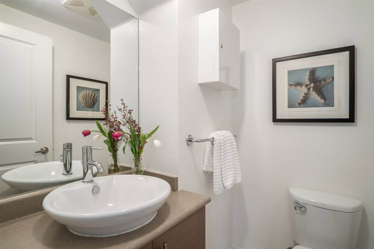 Modern bathroom with white walls, stylish vessel sink, fresh flowers, and framed seaside artwork, showcasing contemporary home design and comfort, perfect for Vancouver Island real estate listings.