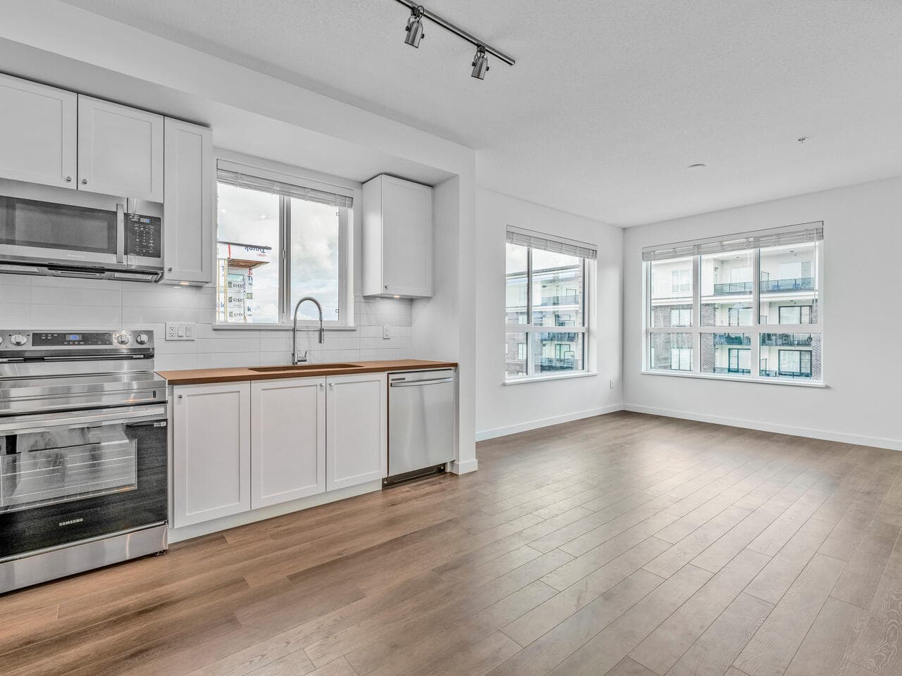 Bright, modern open-concept kitchen and living area in a Vancouver apartment, featuring white cabinetry, stainless steel appliances, large windows, and hardwood floors, ideal for contemporary urban living.