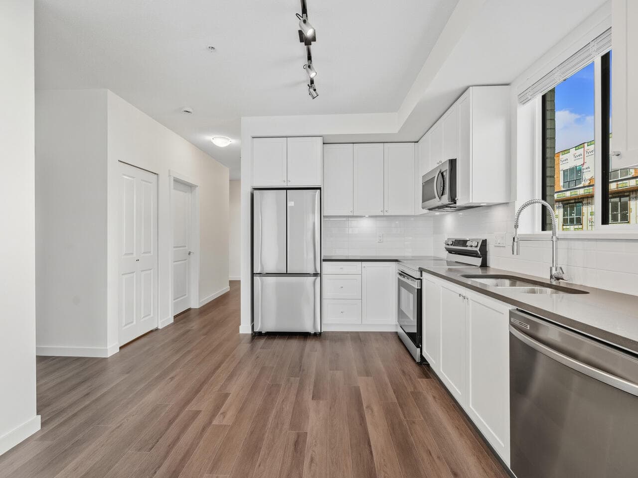 Modern white kitchen with stainless steel appliances and wood flooring, featuring ample cabinetry and natural light, ideal for Vancouver real estate listings.