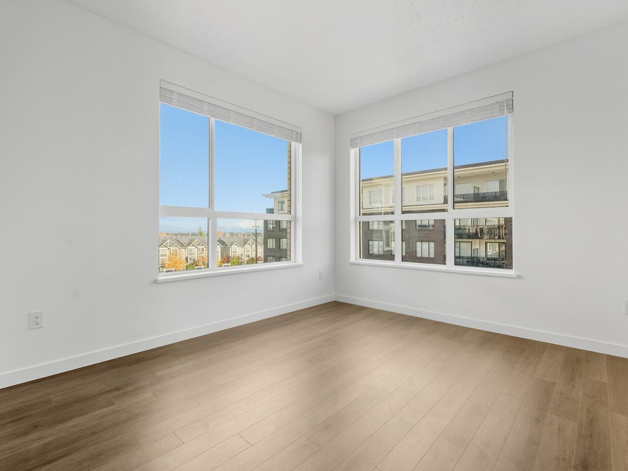 Bright empty room with large windows, white walls, and wood flooring, showcasing modern Vancouver condos for sale by Orca Realty Inc.