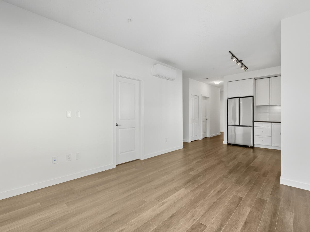Bright modern open-concept living space with white walls, hardwood flooring, and a sleek kitchen highlighting stainless steel appliances, ideal for Vancouver real estate listing.
