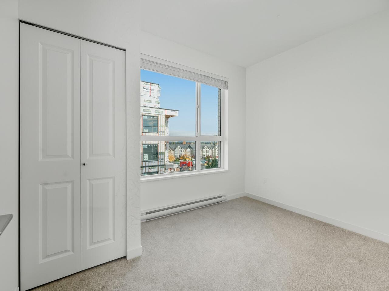 Bright modern bedroom with large window, white walls, neutral carpet, and built-in closet – ideal for Vancouver real estate listings and showcasing property features.