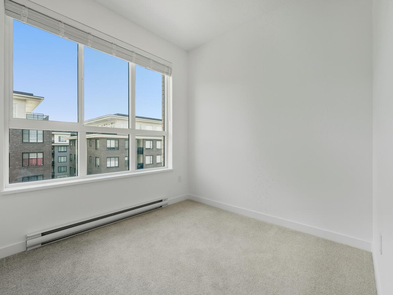 Bright and airy empty bedroom with large windows showcasing city views, ideal for Vancouver condo living. Modern space with neutral carpet and fresh white walls, perfect for personalized interior design.
