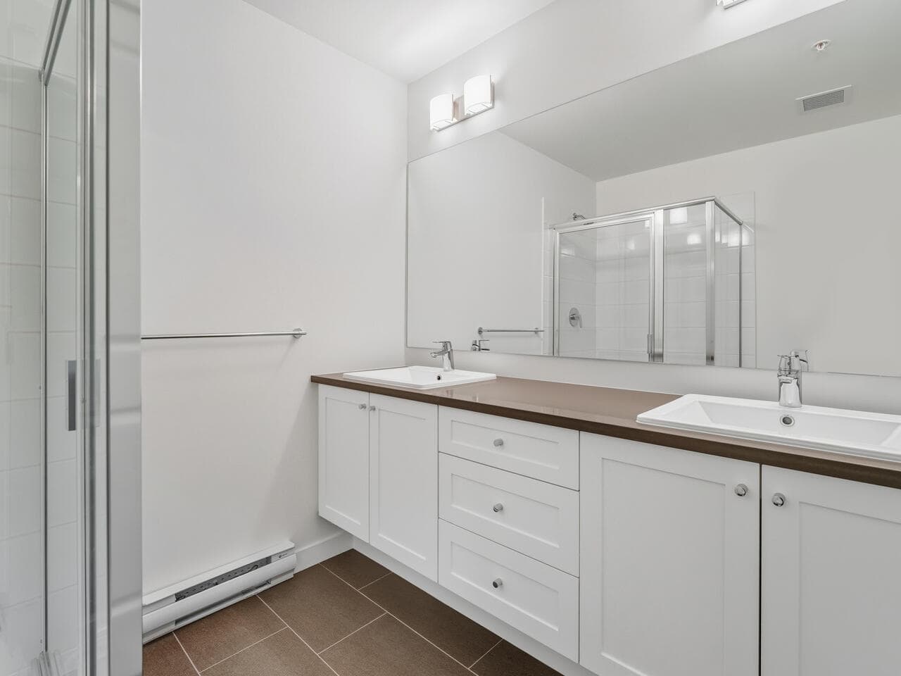 Bright modern bathroom with dual sinks, white cabinets, large mirror, and walk-in shower, part of Orca Realty Inc. property listings in BC, showcasing contemporary home interior design.