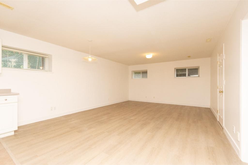 Bright spacious basement with natural light, ideal for Vancouver real estate buyers seeking modern homes, featuring white walls, laminate flooring, and multiple windows for a welcoming atmosphere.