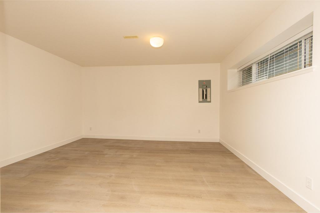 Bright empty basement room with white walls, large window with blinds, and new light fixture, perfect for Vancouver real estate buyers seeking versatile indoor space.