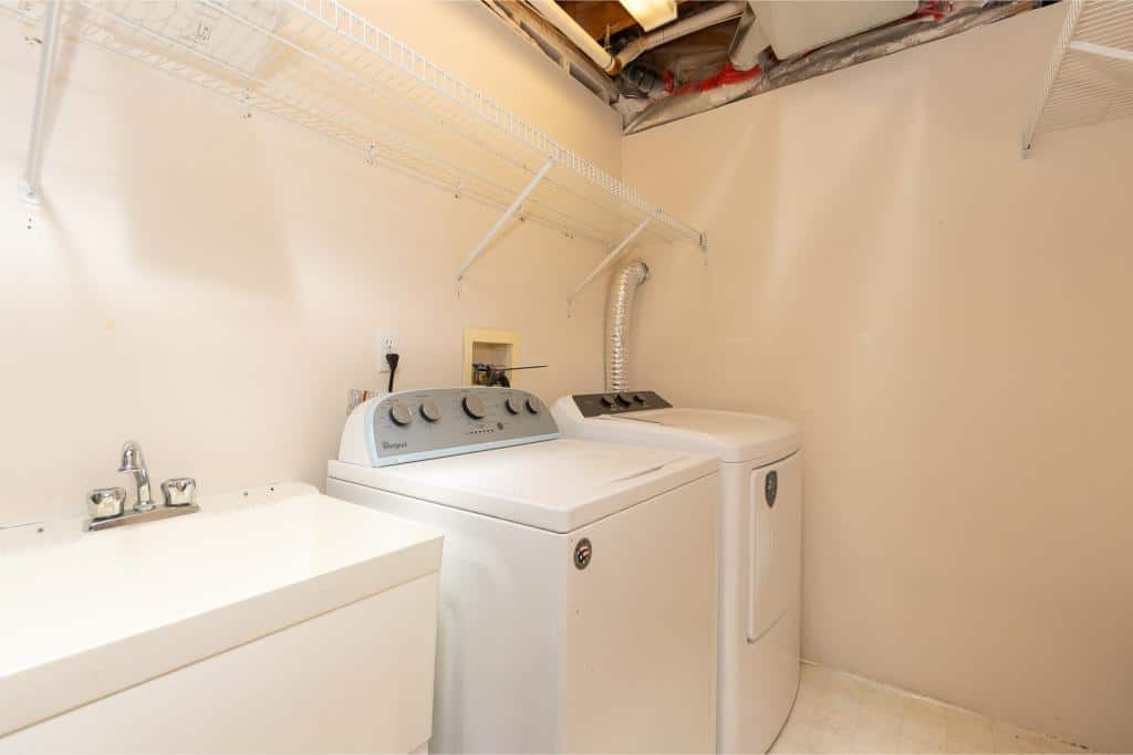 Stacked washer and dryer in a laundry room with utility sink, metal shelving, and exposed ceiling pipes, highlighting in-home laundry solutions by Orca Realty Inc.