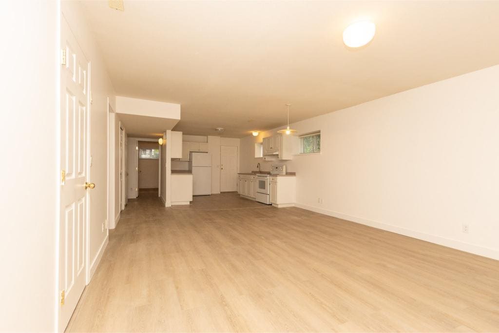 Spacious open-concept living area with modern kitchen, ideal for Vancouver Island homes, featuring light wood flooring, white cabinetry, and natural light for a bright, inviting space.