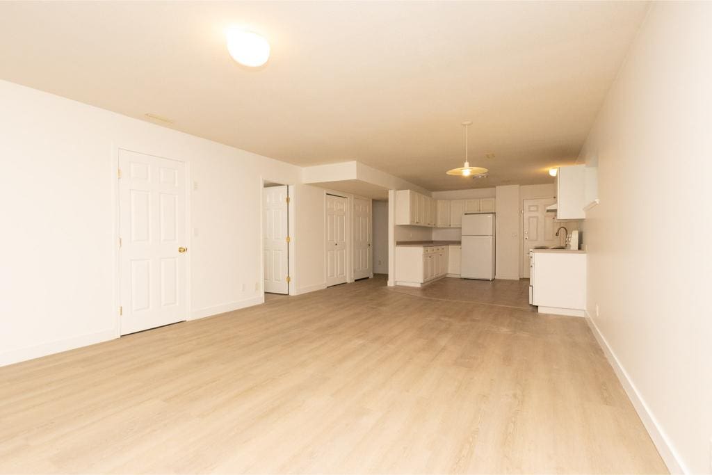 Bright and spacious open-concept apartment in a clean, modern building with white kitchen cabinets, laminate flooring, and ample natural light, ideal for Vancouver-area homebuyers and renters.
