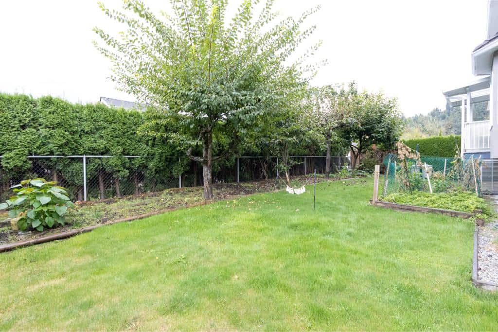 Lush residential backyard with well-maintained lawn, mature trees, garden beds, and privacy fencing in a Vancouver Island community.