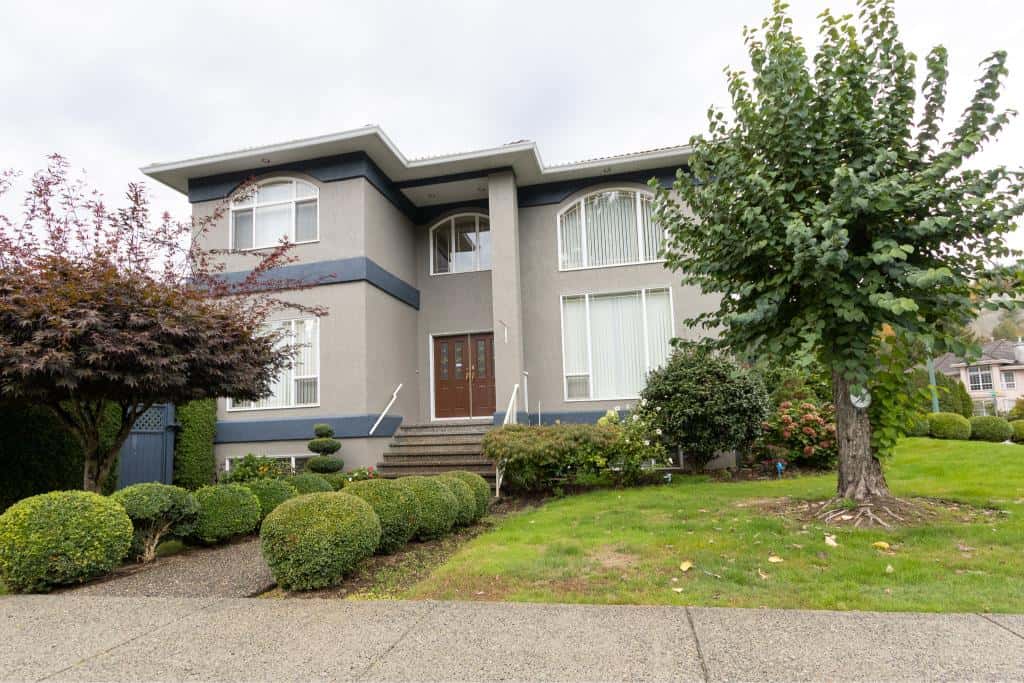 Modern grey two-story house with well-maintained landscaping, mature trees, and lush green lawn in a suburban neighbourhood in Vancouver, British Columbia.