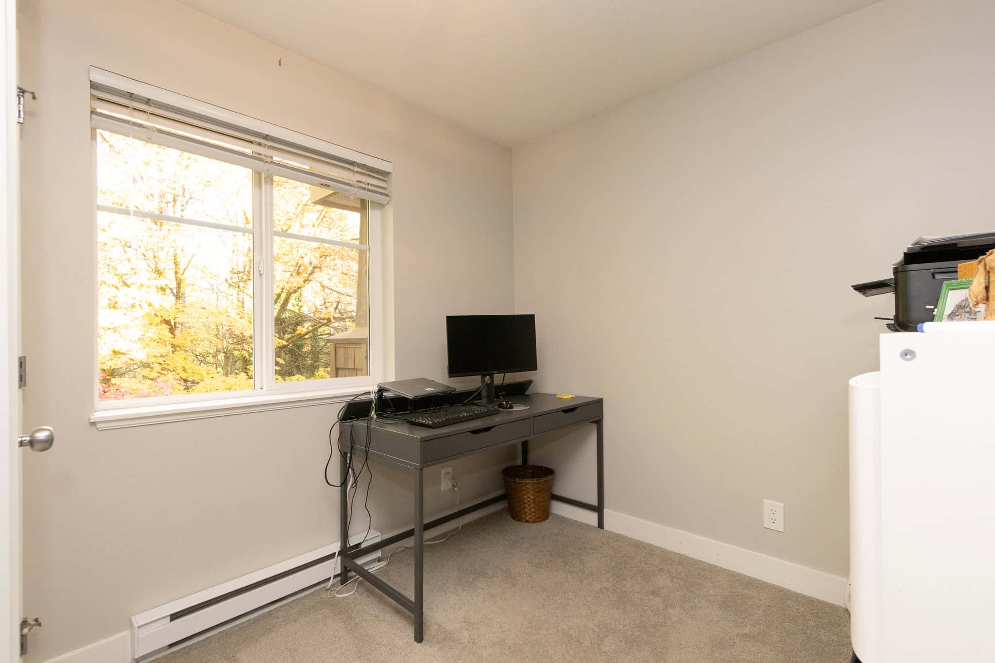 Cozy home office with a desk, computer, and window view of autumn trees, perfect for remote work or study.