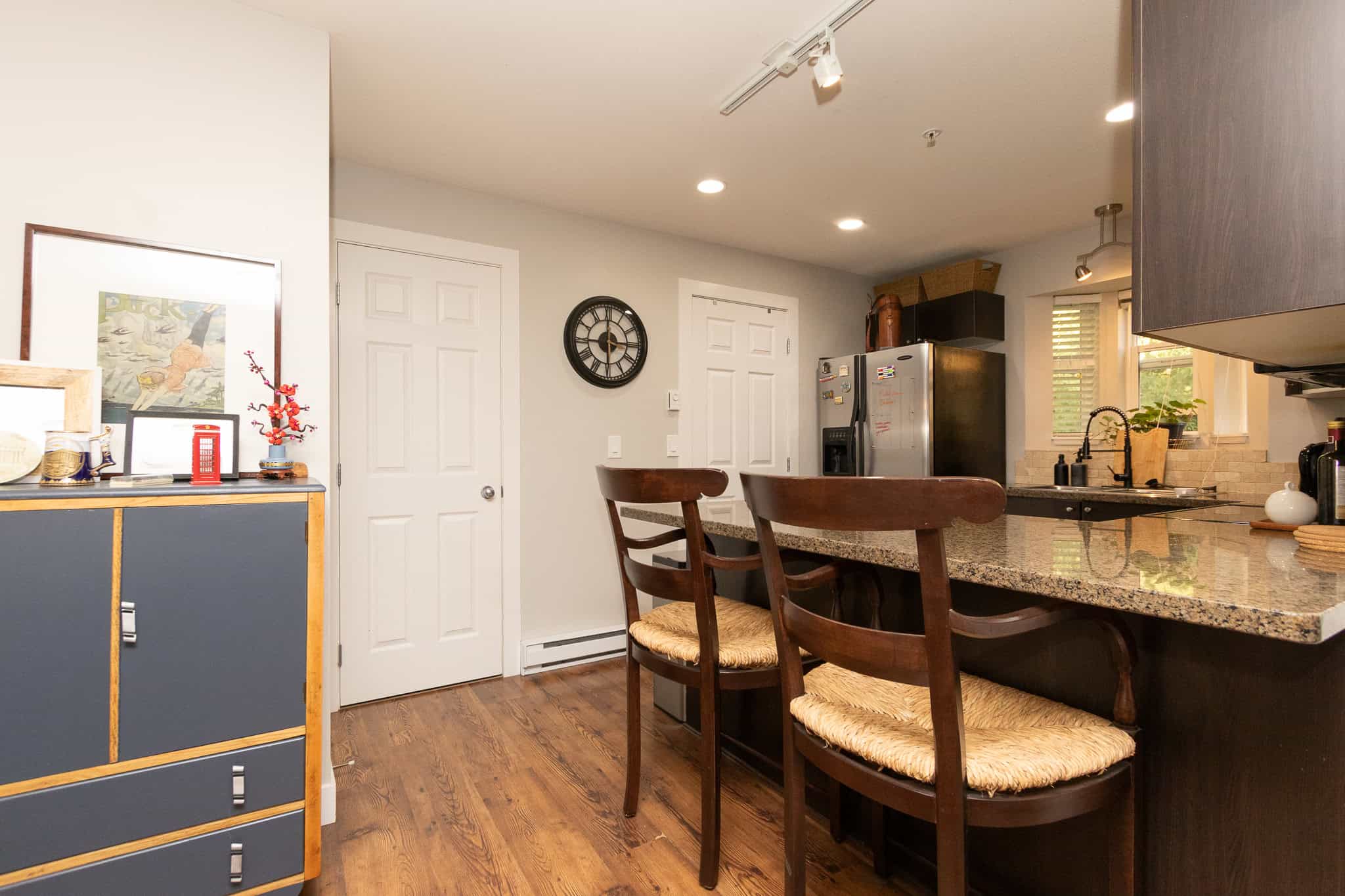 Bright modern kitchen with granite countertops, stainless steel appliances, and breakfast bar, featuring ample natural light and contemporary design – ideal for Vancouver Island real estate.