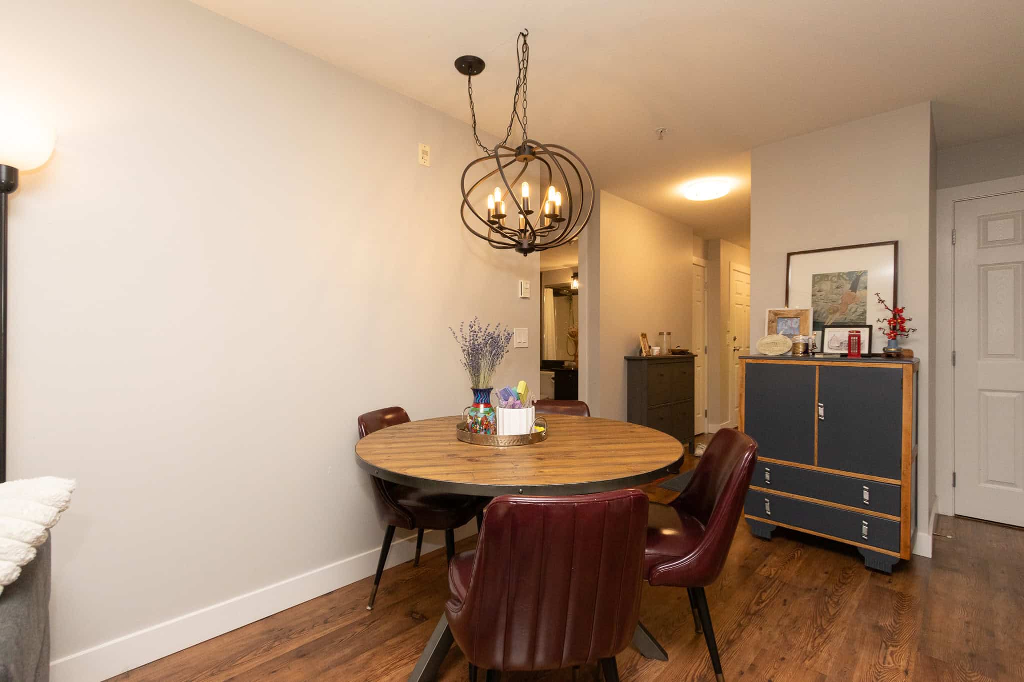 Modern dining room with wood flooring and stylish chandelier anchoring the space. Comfortable leather chairs around a round wooden table, perfect for family meals or entertaining guests.