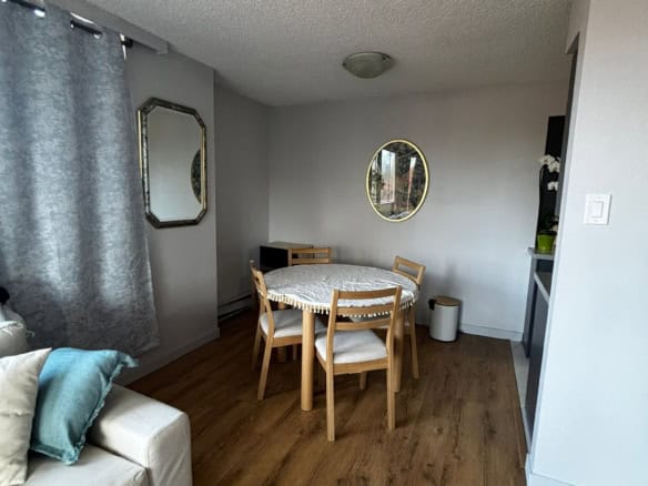 Cozy dining area with round wooden table, four chairs, and natural light from window with grey curtains, in a modern home interior.
