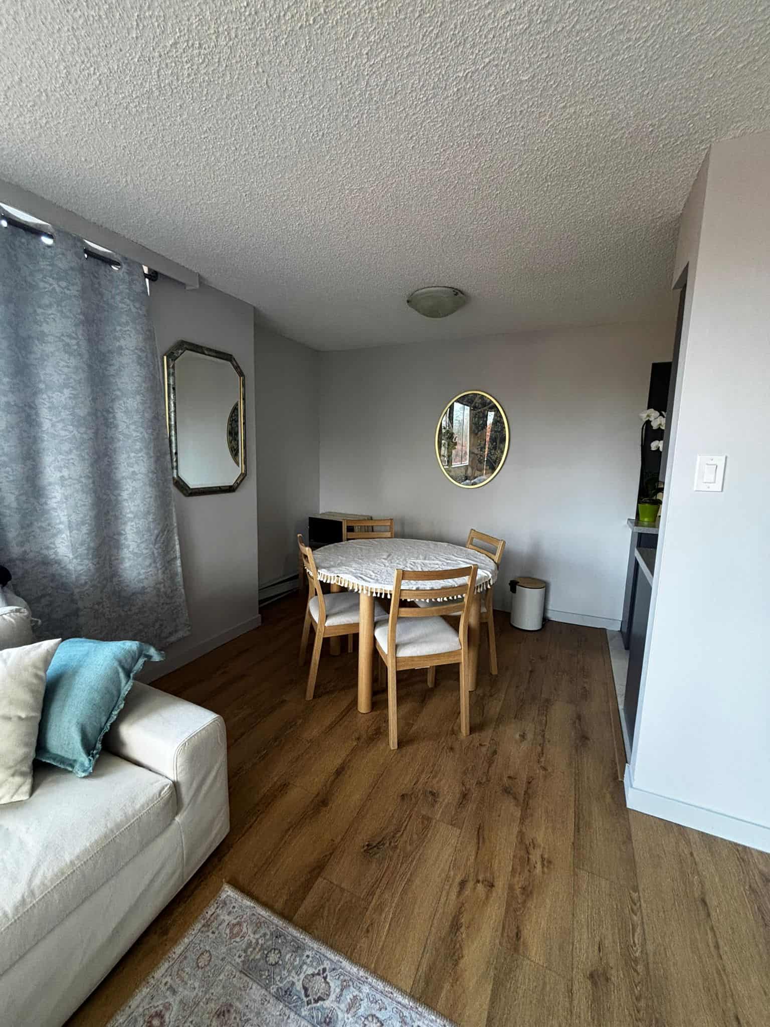 Cozy dining area with round wooden table, four chairs, and natural light from window with grey curtains, in a modern home interior.