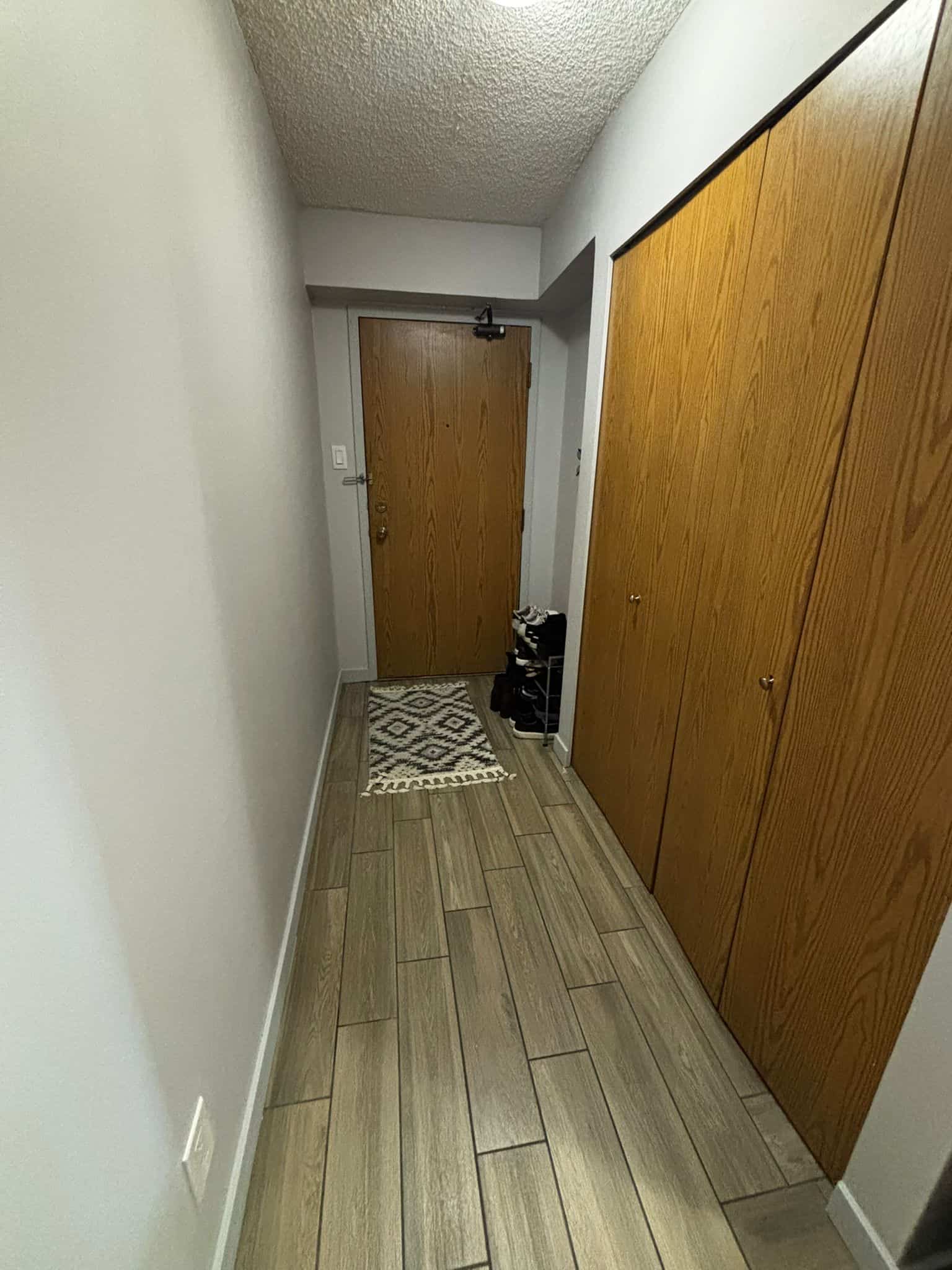 Cozy apartment entryway with wooden closet doors, a front door with security latch, and a small patterned rug on wood-look tile flooring, showcasing safe and functional interior real estate features.