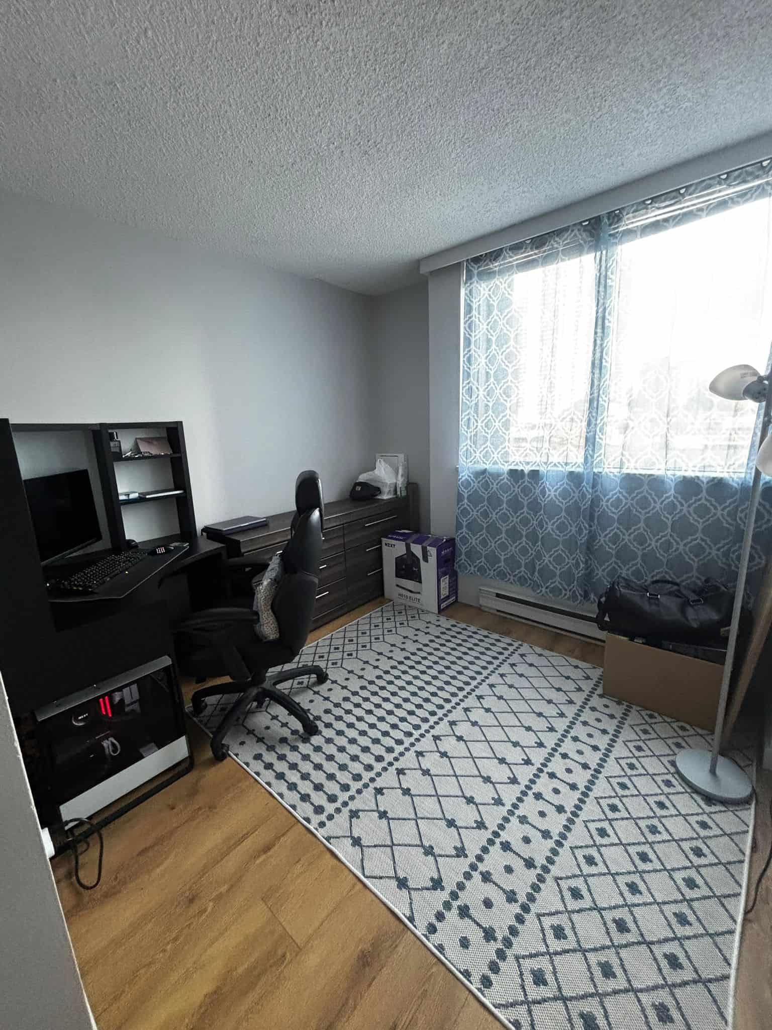 Modern home office with desk, ergonomic chair, window with patterned curtains, and hardwood flooring, ideal for remote work or studying.