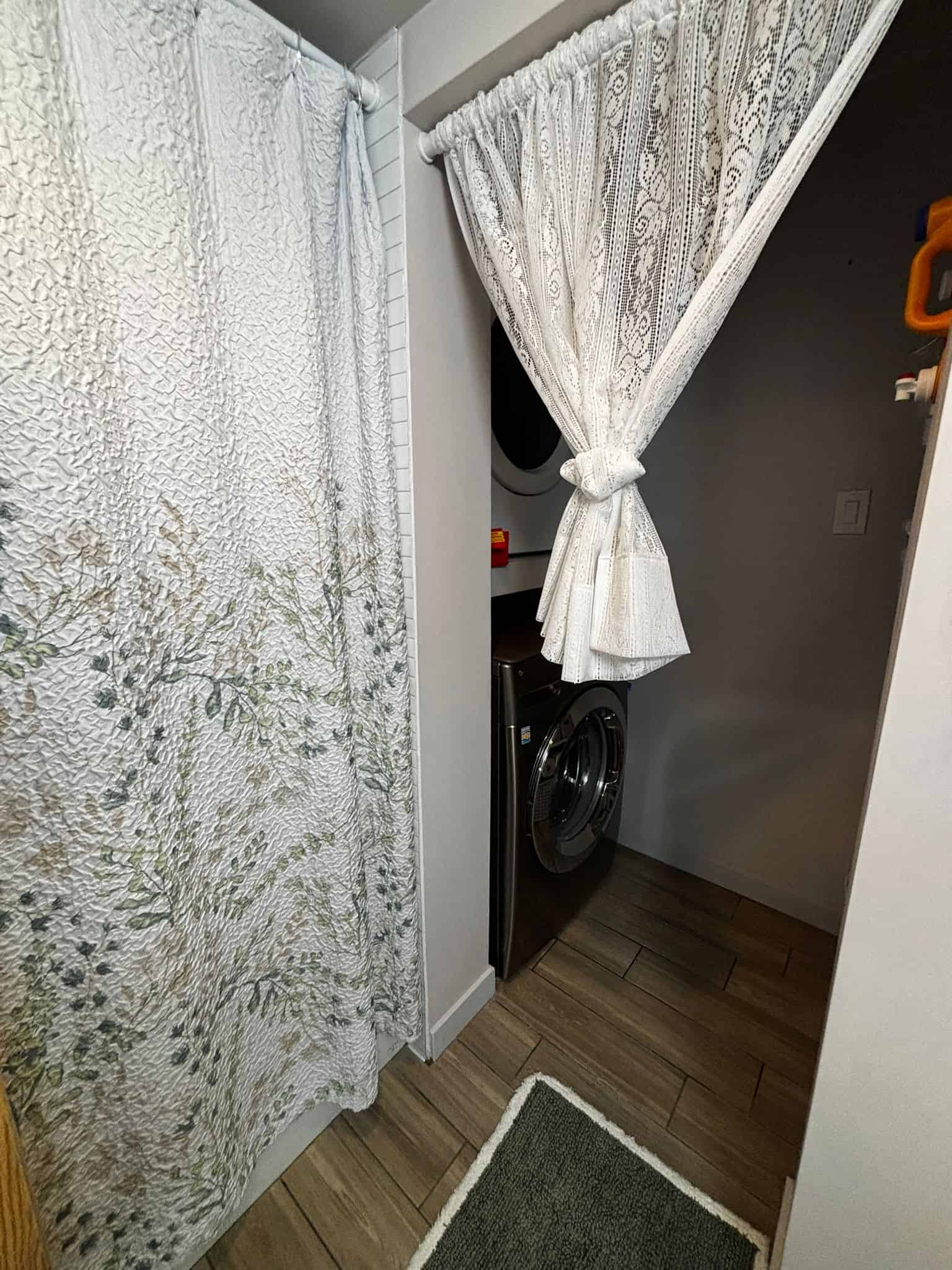 Compact laundry area with washer and dryer, enclosed by decorative lace curtains, in a modern home listing by Orca Realty Inc., located in Victoria, BC.