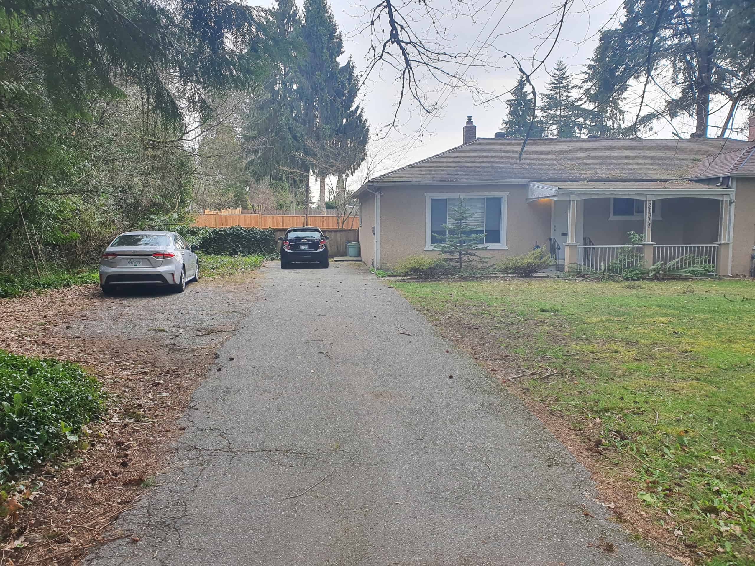 Spacious driveway leading to a single-story house with front porch, surrounded by trees and greenery, ideal for suburban living in the Vancouver area.