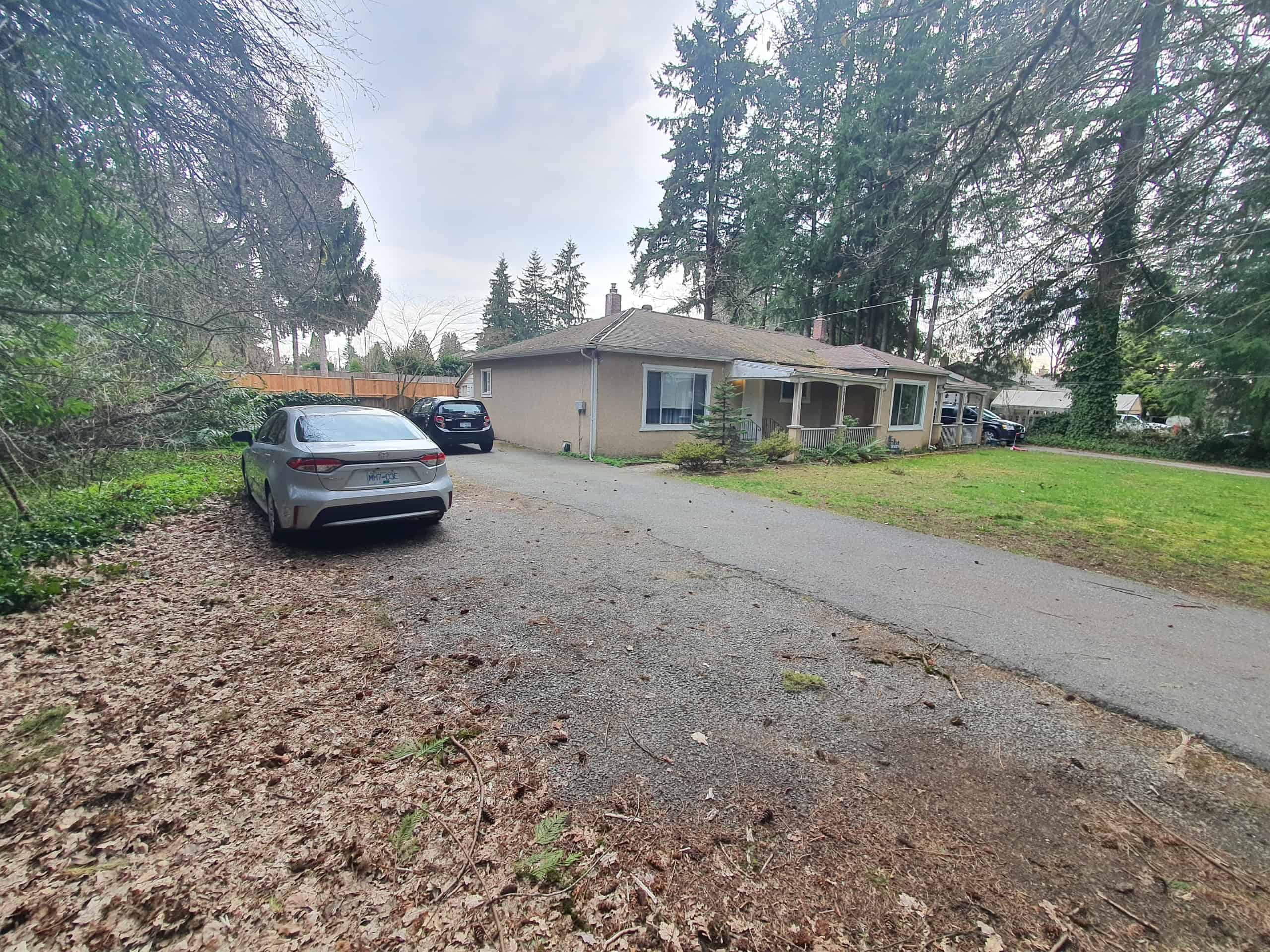 Bright, spacious single-story home with a large driveway, surrounded by tall trees and lush greenery, offering a peaceful residential setting in Orca Realty Inc. service area.