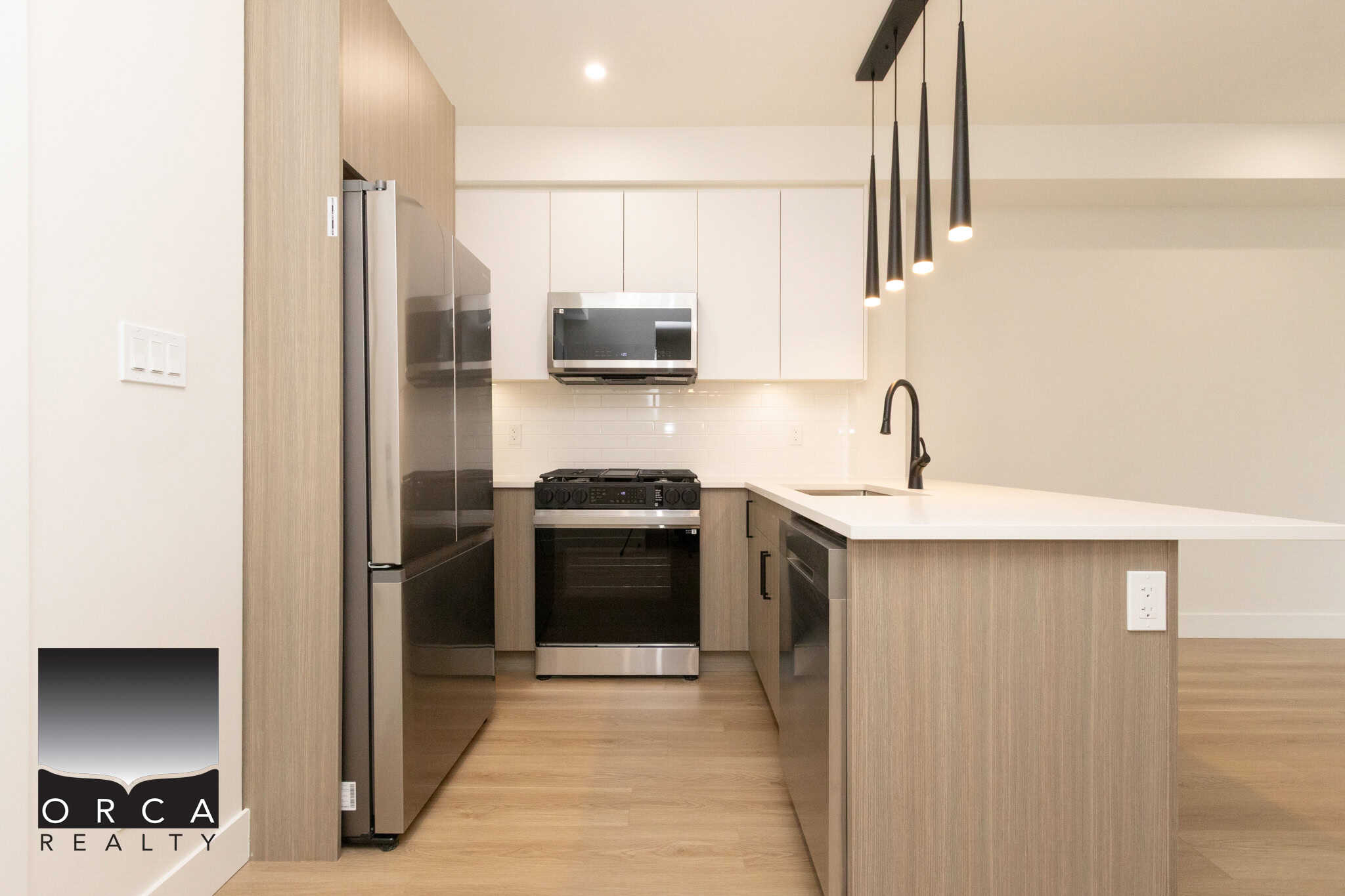 Modern kitchen with stainless steel appliances, white cabinetry, and minimalist black pendant lighting, showcasing contemporary interior design for Vancouver Island real estate.