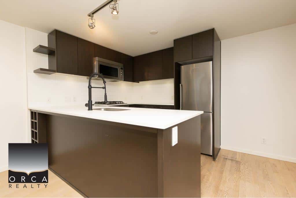 Contemporary modern kitchen with stainless steel appliances, dark wood cabinets, white countertop, and minimalist design. Perfect for stylish urban living and real estate opportunities in Vancouver.