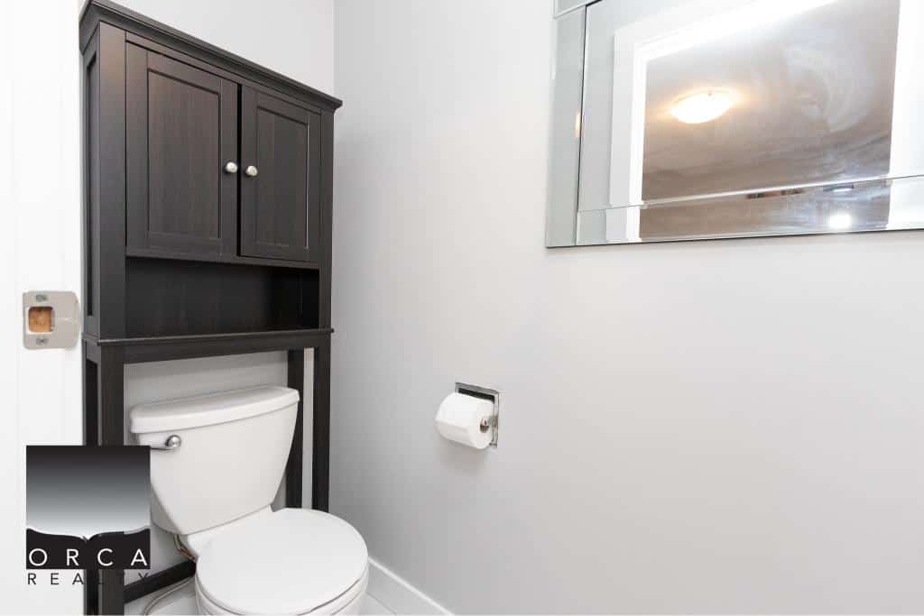 Modern bathroom with white fixtures, dark wood cabinet, and wall-mounted mirror in a contemporary home.