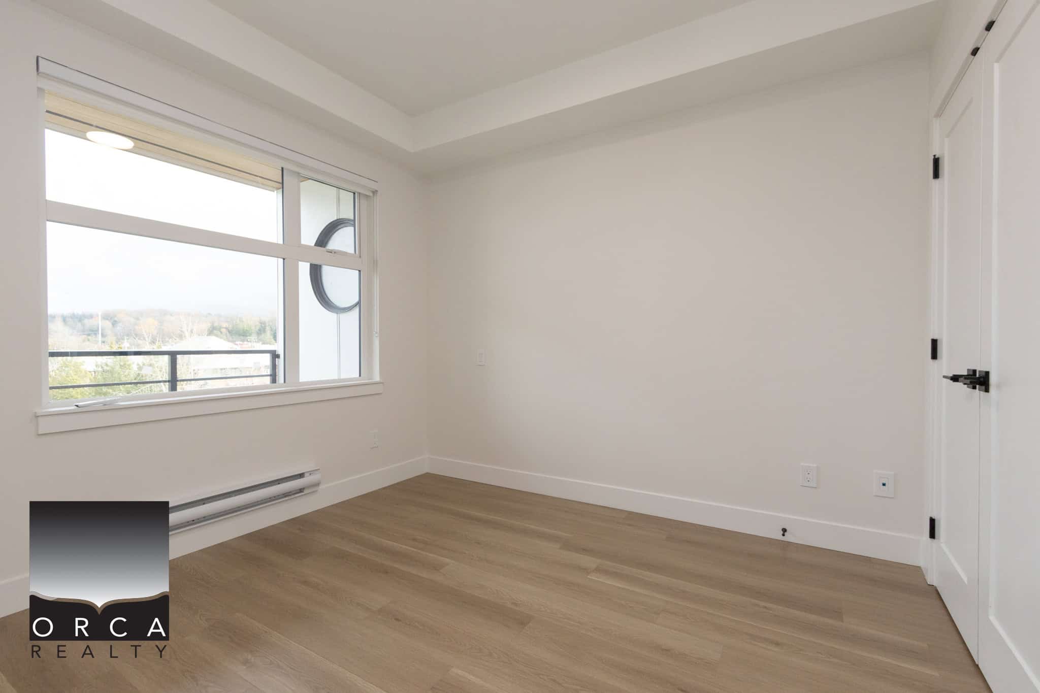 Bright modern empty bedroom with large window, beige wooden flooring, white walls, closet, and natural light, ideal for Vancouver real estate or condo listings.
