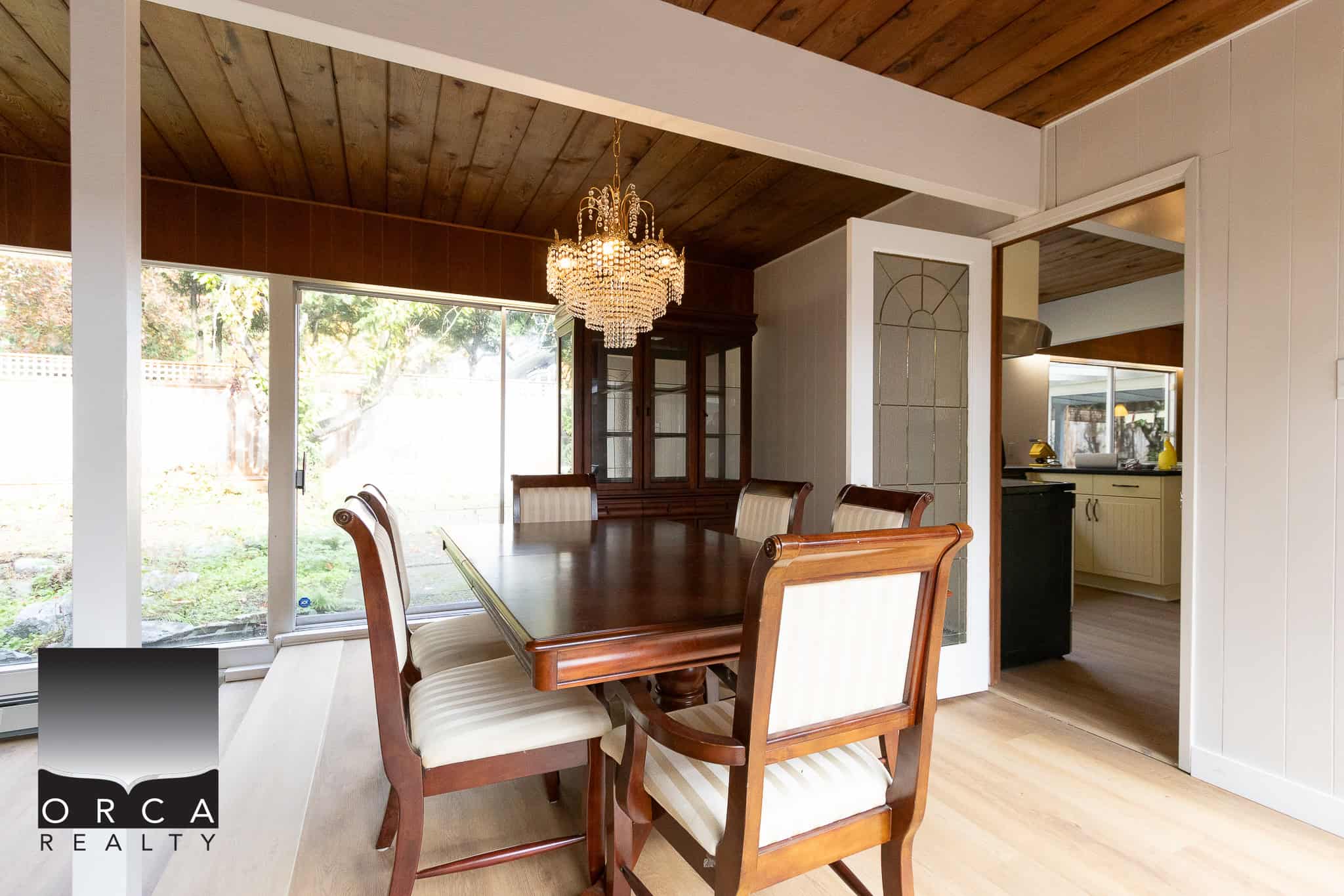 Elegant dining room featuring a classic wooden dining table with six upholstered chairs, a stunning chandelier, and large sliding glass doors that lead to a private backyard garden.