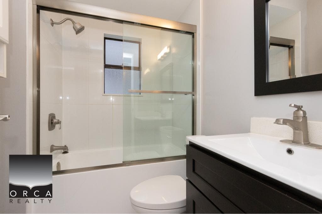 Modern bathroom with glass shower enclosure, white bathtub, black vanity, and contemporary fixtures, perfect for Vancouver Island real estate listings.