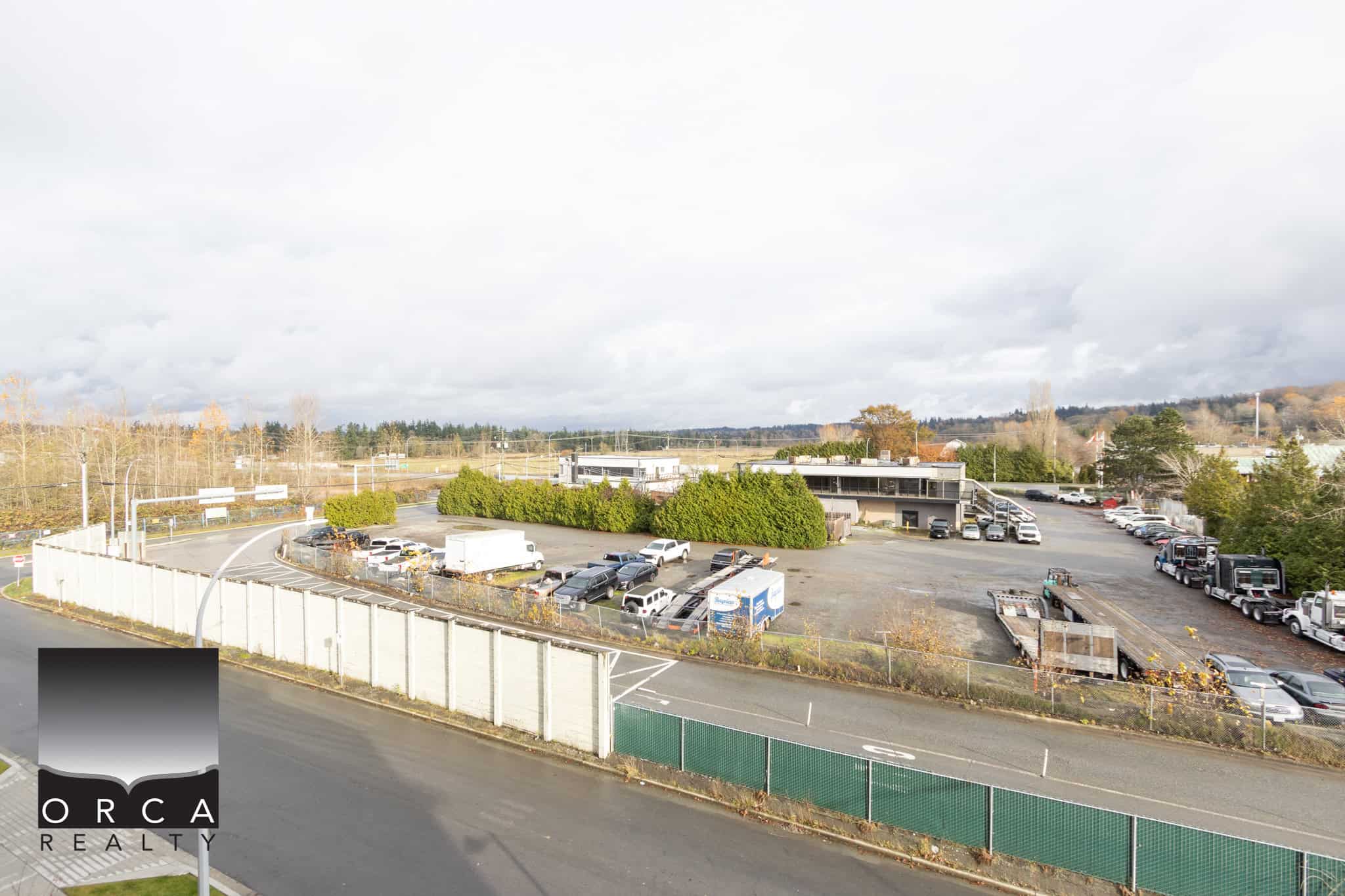 Aerial view of commercial property with parking lot, office building, trucks, and surrounding landscape, highlighting Orca Realty's Vancouver Island real estate services and property management expertise.